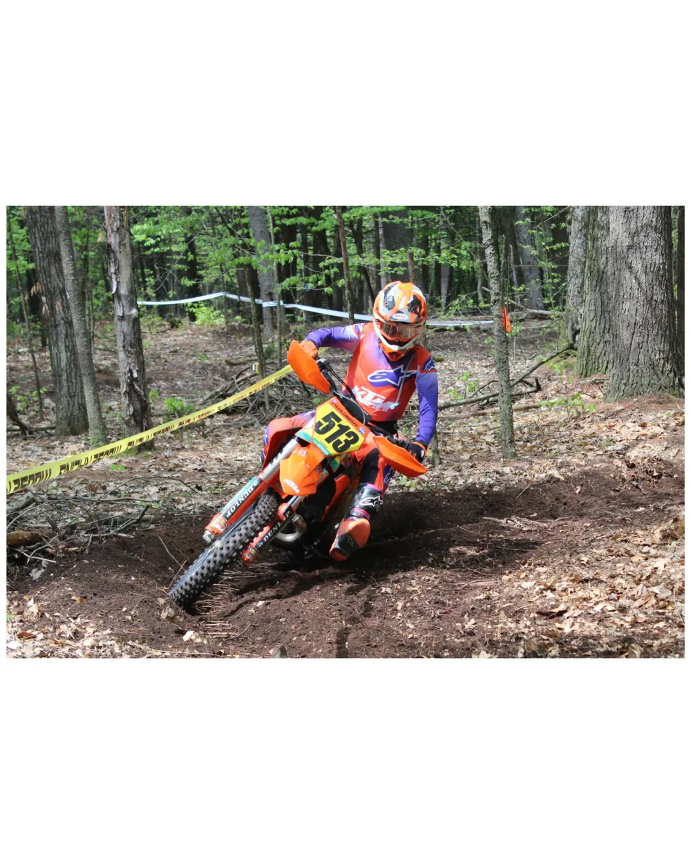 Motocross rider numbered 573 leaning through a dirt corner in the woods
