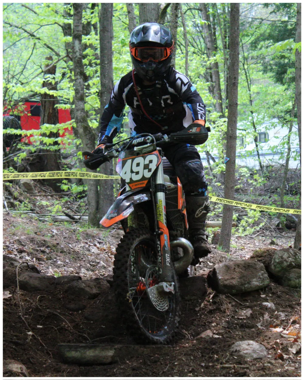 Motocross rider numbered 492 navigating a rocky section of a wooded course