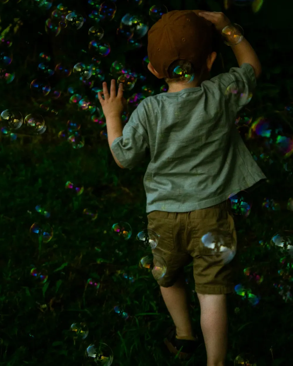 Young child walking through grass while surrounded by floating soap bubbles