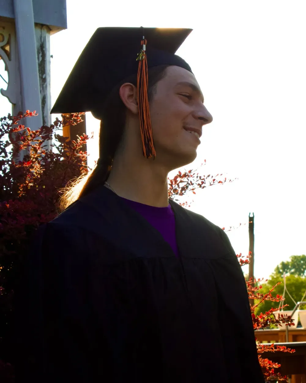 Graduate wearing a cap and gown outdoors in warm evening light